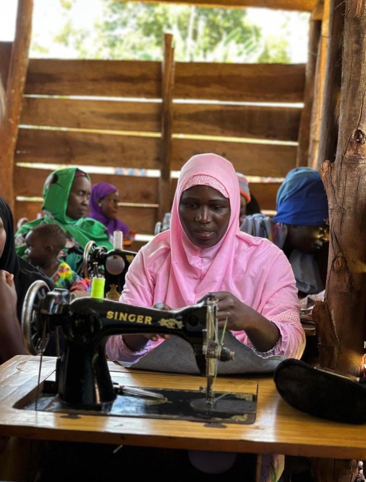 A Musana graduate tailoring on a Singer sewing machine, surrounded by fellow trainees
